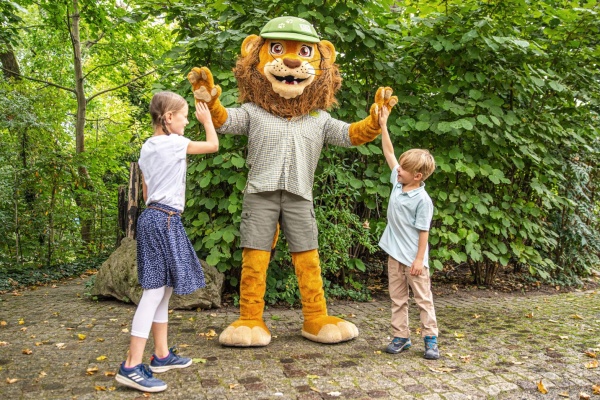 zwei Kinder geben Zoo-Maskottchen Tammi ein High-Five